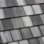 Close-up view of a roof with overlapping, rectangular gray shingles in varying shades, creating a striped pattern.