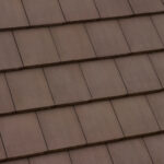 A close-up view of a brown tiled roof with overlapping rectangular tiles arranged in neat, horizontal rows.