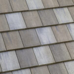 Close-up view of several rows of beige and gray concrete roof tiles, arranged in overlapping horizontal lines, showing the texture and pattern of the shingles.