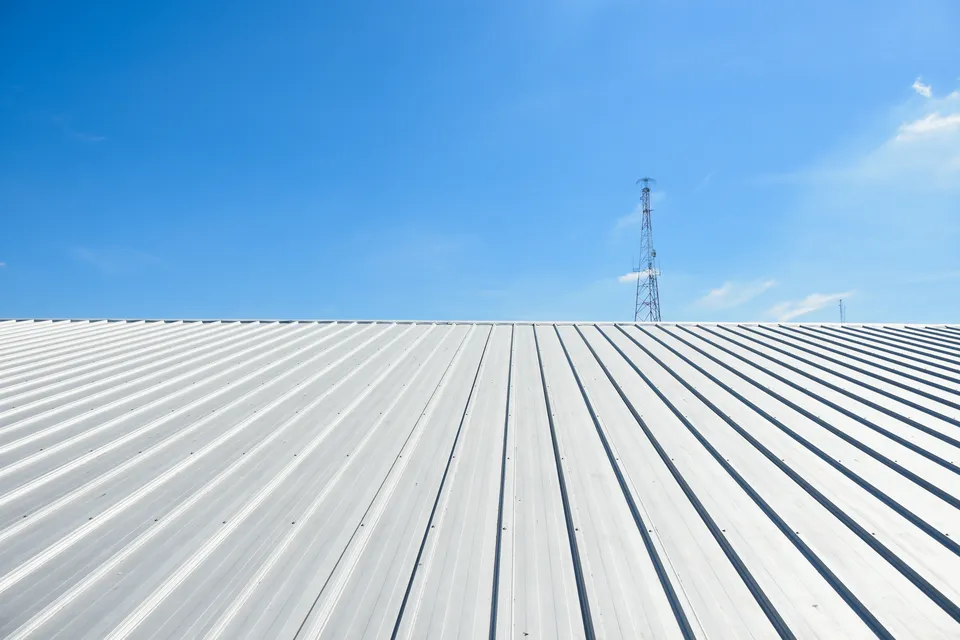 A bright, clear sky above a large, clean, white metal roof with visible ridges; a tall communication tower stands in the background.