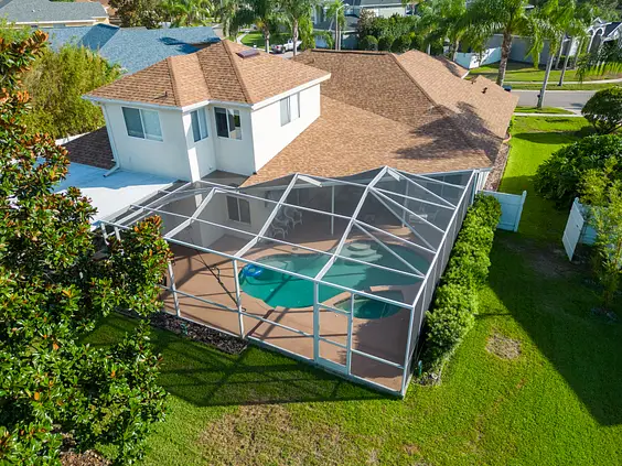 Aerial view of a house with a screened-in patio and backyard pool, surrounded by green grass, trees, and neighboring homes—showcasing quality roofing Valrico residents can trust.