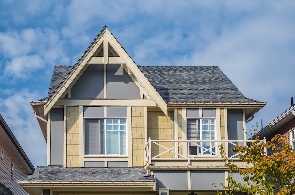 Two-story house with a peaked roof, large front-facing windows, beige and gray siding, white trim, and a small balcony—an inviting example of roofing Citrus Park style against a partly cloudy blue sky.