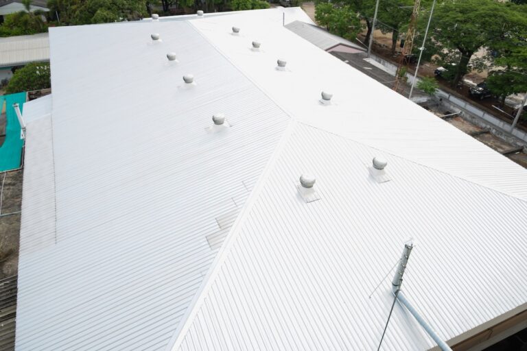 A large white metal roof with multiple ventilation turbines, viewed from above, showcases expert commercial roofing in Palm Harbor. Trees and nearby buildings are visible along the edges of the roof.